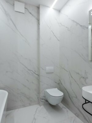 Interior of contemporary bathroom with white bath placed near toilet and washbasin at wall with mirror with reflection at home